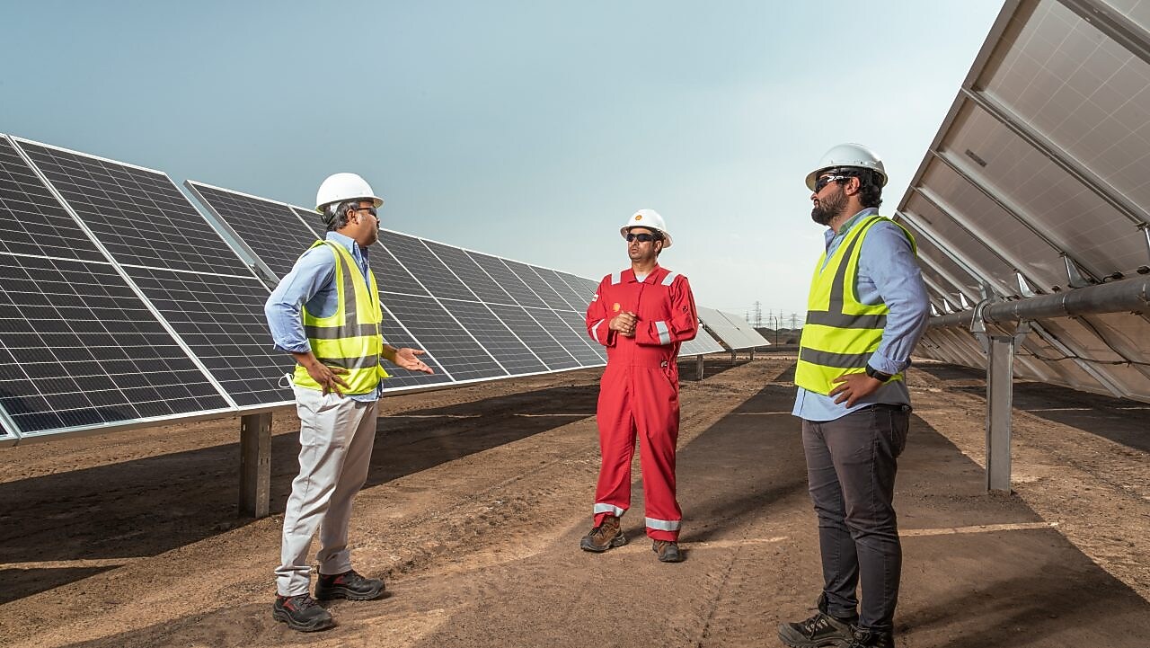 Três homens conversando em um corredor com placas solares em volta