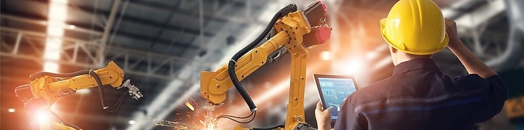 Técnico ao trabalho em uma planta industrial operando dois braços robóticos