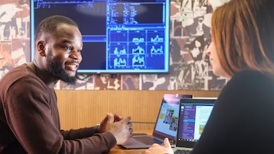 Jovem mulher de óculos aponta para uma tela exibindo alguns gráficos