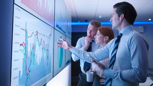 dois homens e uma mulher discutem os gráficos exibidos em uma tela.