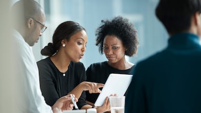 Duas mulheres e um homem conversam ao redor de uma mesa