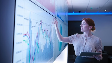 Mulher aponta para um gráfico exibido em uma tela.