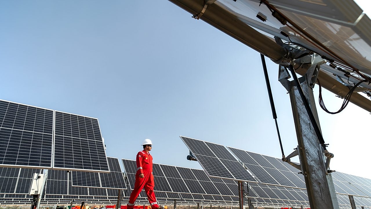 operário caminha entre painéis de geração solar
