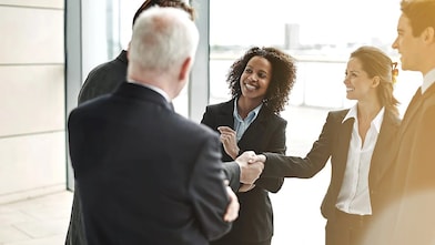 Grupo de homens e mulheres vestindo traje social se cumprimentando