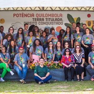 Foto coletiva com cerca de 30 pessoas sorridentes, reunidas em frente a um painel com a frase: “Potência Quilombola: Terra Titulada, Direito Conquistado”.