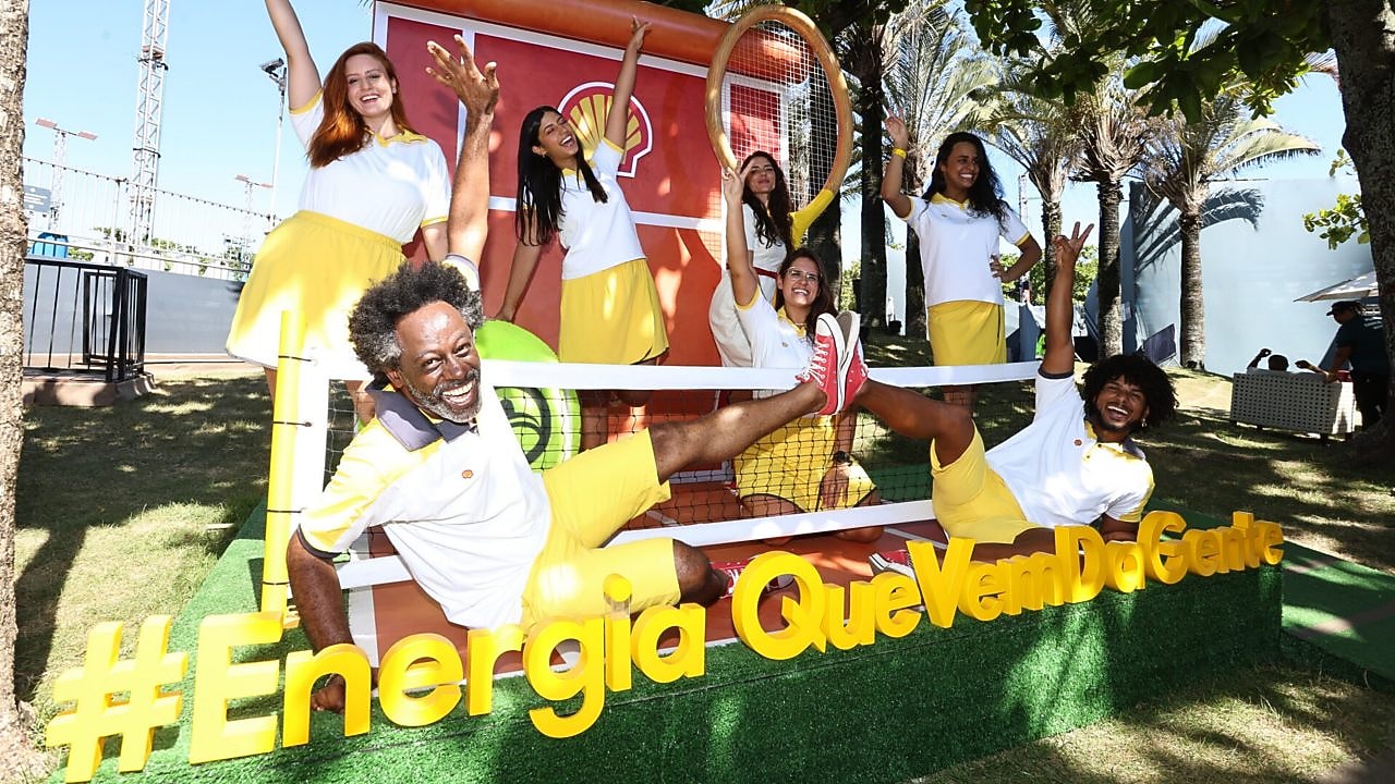 Instalação visual iluminada mostra o desenho de um cérebro com o logotipo da Shell ao centro, enquanto silhuetas de pessoas caminham ao fundo.