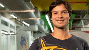 Um homem de blusa preta, segurando uma placa amarela e  sorrindo.