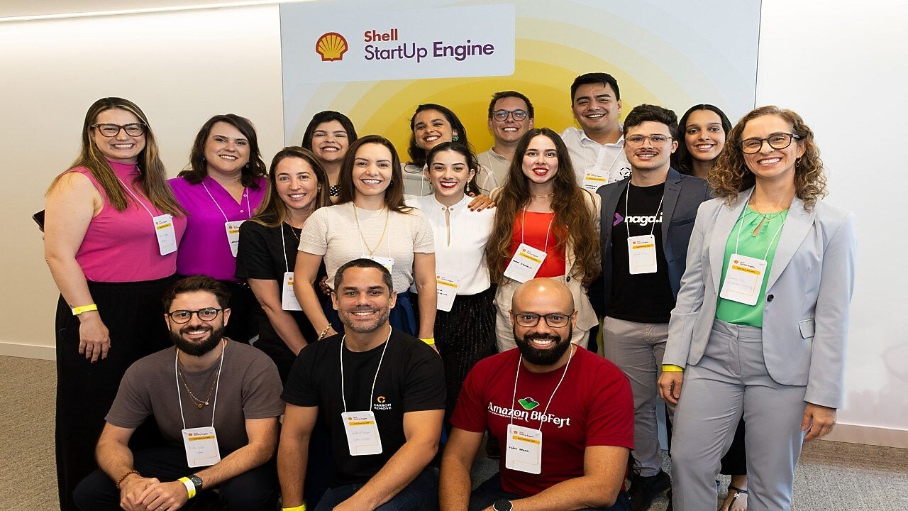Grupo de pessoas sorrindo em frente a um painel com logotipos de um evento de premiação