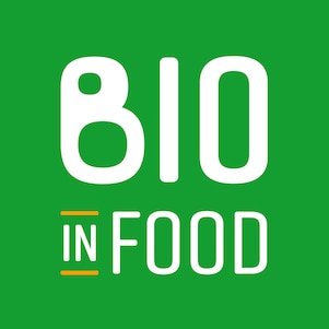 Logotipo da marca "Bio in Food" com fundo verde. A palavra "BIO" aparece em letras brancas grandes na parte superior, e a palavra "FOOD" está logo abaixo, também em branco. A palavra "IN", centralizada entre ambas, está em branco com sublinhado duplo em laranja.