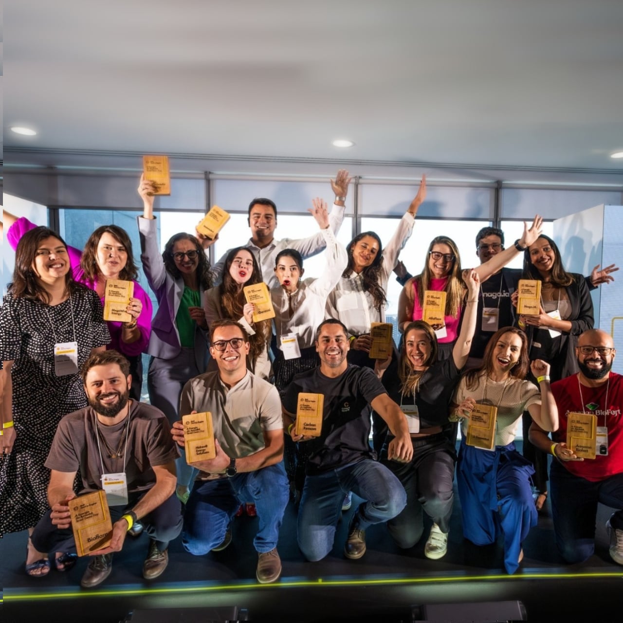 Grupo de pessoas sorrindo em frente a um painel com logotipos de um evento de premiação