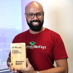 Homem negro sorrindo enquanto segura um troféu de madeira.