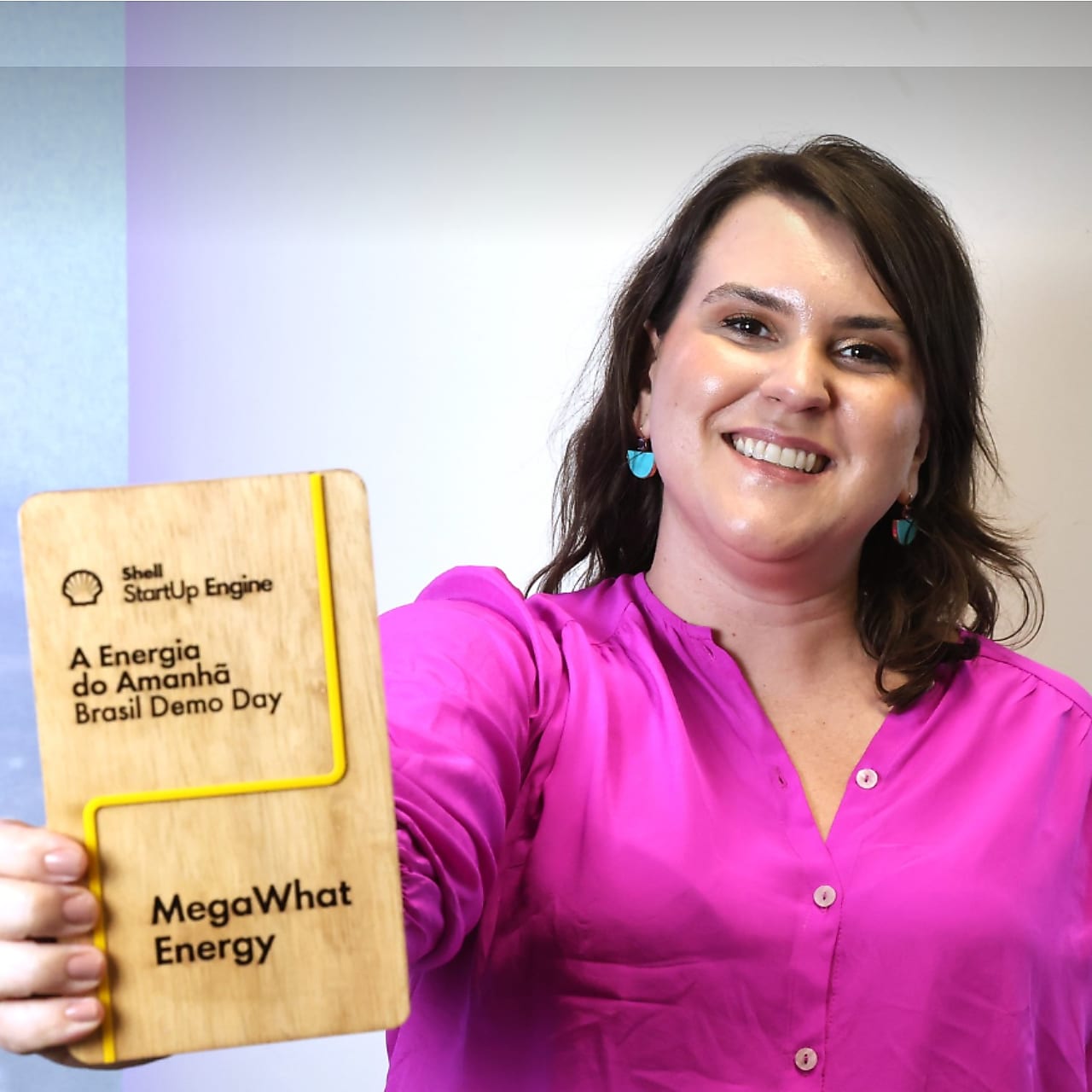 Mulher branca, de cabelos escuros, sorrindo enquanto segura um troféu de madeira.