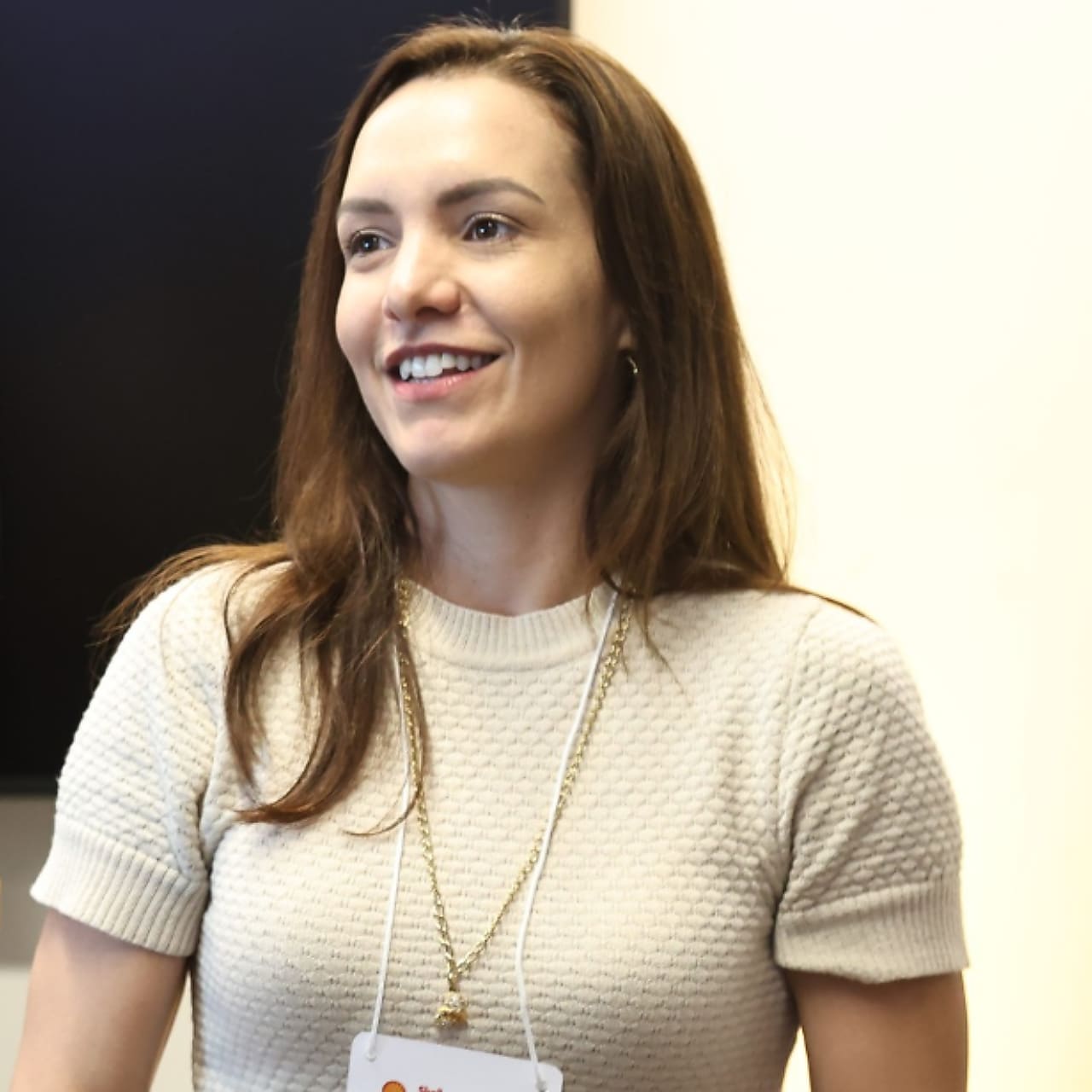 Mulher branca sorrindo, vestindo uma blusa bege, em um fundo neutro.