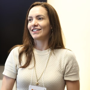 Mulher branca sorrindo, vestindo uma blusa bege, em um fundo neutro.