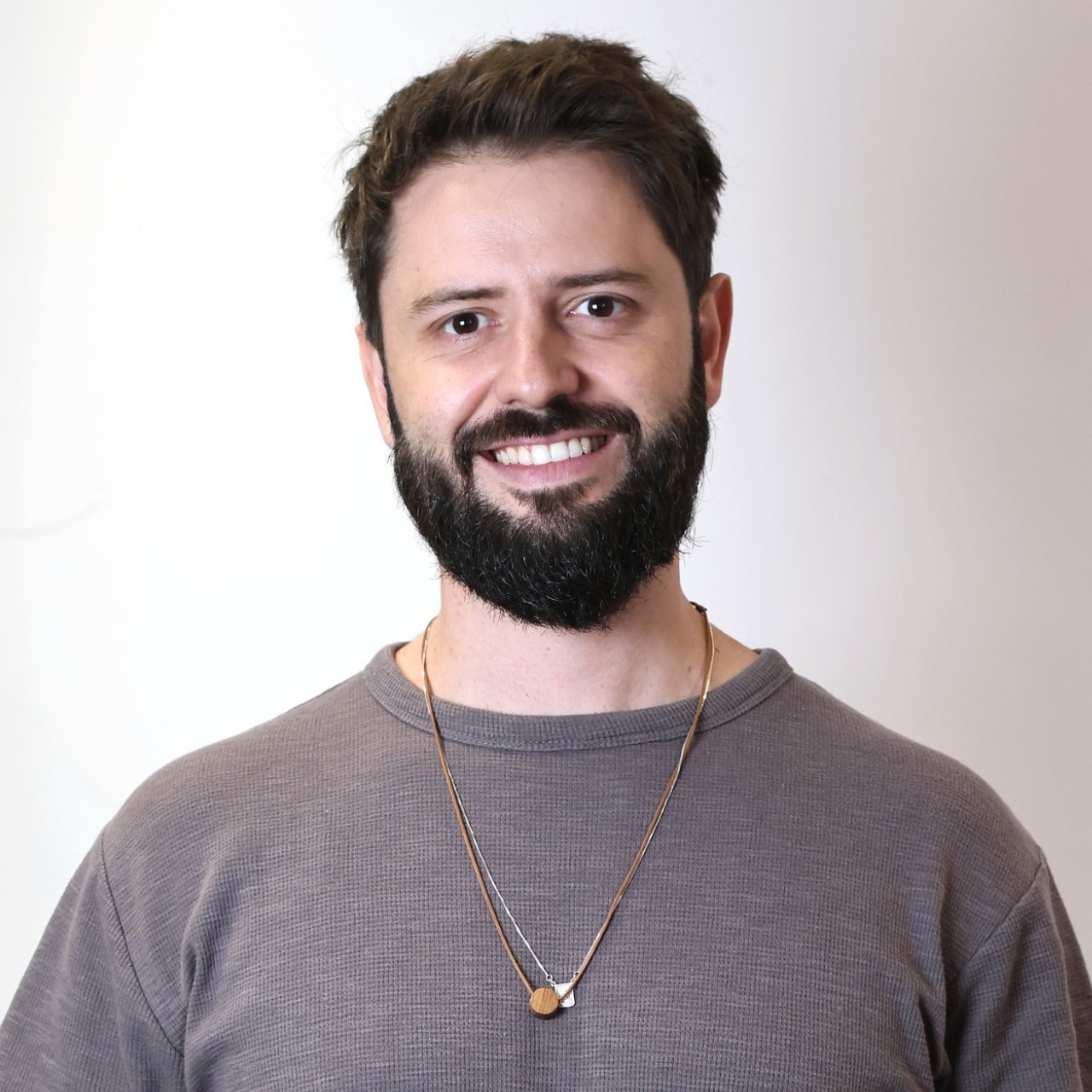 Homem, branco e de camisa cinza, sorrindo em um fundo branco.